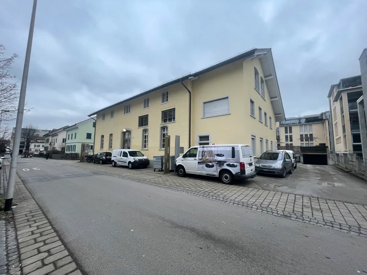 Ein gelbes Gebäude mit zwei weissen Lieferwagen und anderen Autos davor. 